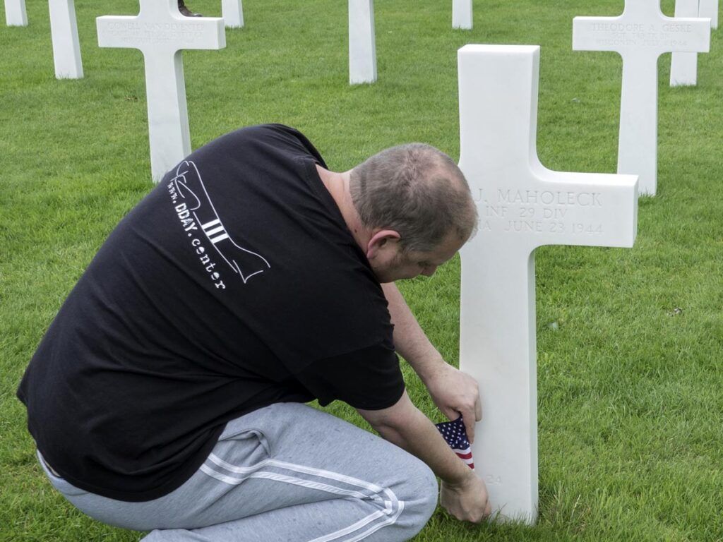 Man Placing American Flag At Base Of White Cross